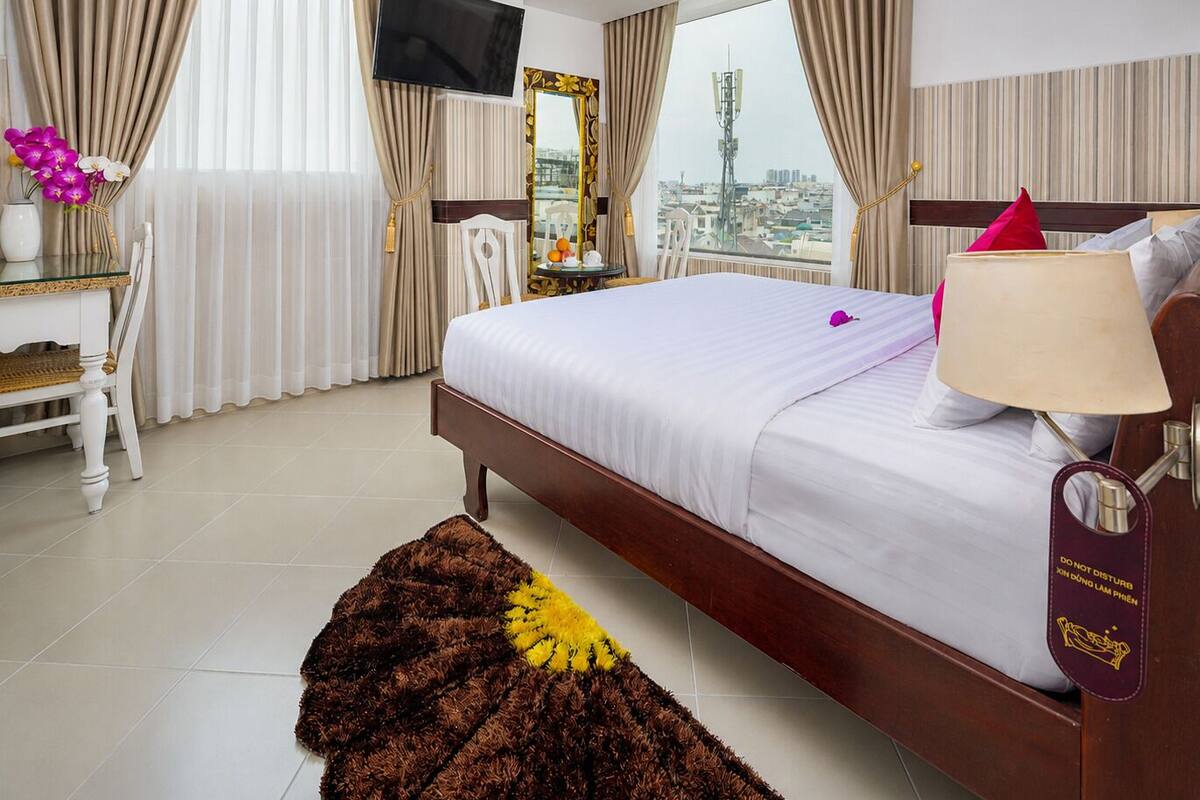 Une chambre d’hôtel comprenant un lit, une télévision, un bureau avec une chaise, une fenêtre avec des rideaux et une vue sur la ville.