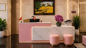 A reception desk with a framed painting, a reception sign, and a flag. - Pink Suite Saigon Airport Hotel (Ho Chi Minh City)