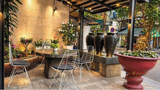 An outdoor seating area with a round table and chairs, surrounded by potted plants and large vases. - Pink Suite Saigon Airport Hotel (Ho Chi Minh City)