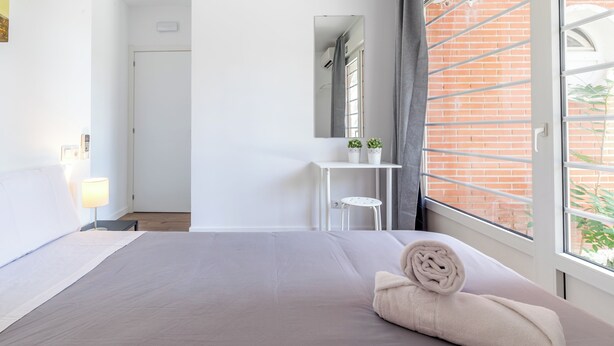 Camera d'albergo moderna con un letto grande, una piccola scrivania, uno specchio e una finestra che si affaccia su un edificio in mattoni.
