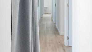 Un corridoio con una tenda grigia, pareti bianche e un pavimento in legno chiaro.