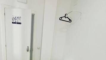 A hotel room with a bed, a white door, a white wall, a white chair, and a white table.
