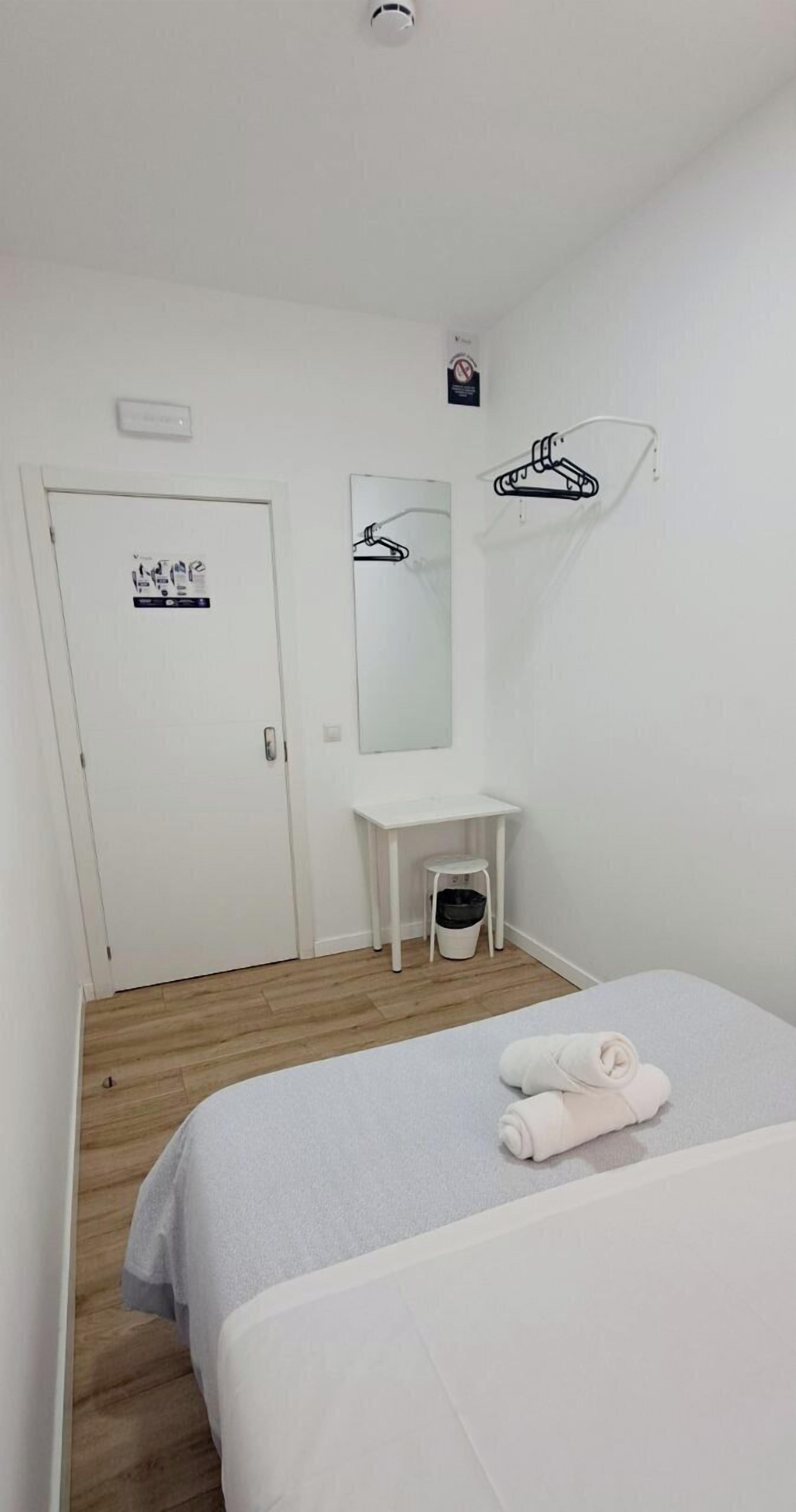 Una habitación de hotel con una cama, un pequeño escritorio, un espejo y una puerta.