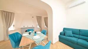 A modern living room with a teal sofa, a dining table with chairs, and a kitchen area visible through an archway. - Villa Aida Luxury Apartments & Spa (Forio)