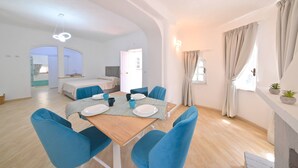 A modern, well-lit room with a dining table set for four, blue chairs, a bed, and a fireplace. - Villa Aida Luxury Apartments & Spa (Forio)