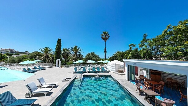 A pool area with lounge chairs and umbrellas, a bar area with tables and chairs, and a clear blue sky. - Villa Aida Luxury Apartments & Spa (Forio)