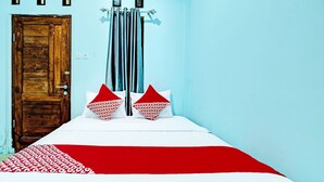 A room with a wooden door, a bed with a red and white bedspread, two pillows with red and white patterns, and a blue wall. - OYO 91987 Archery Residence Syariah (Sewon)