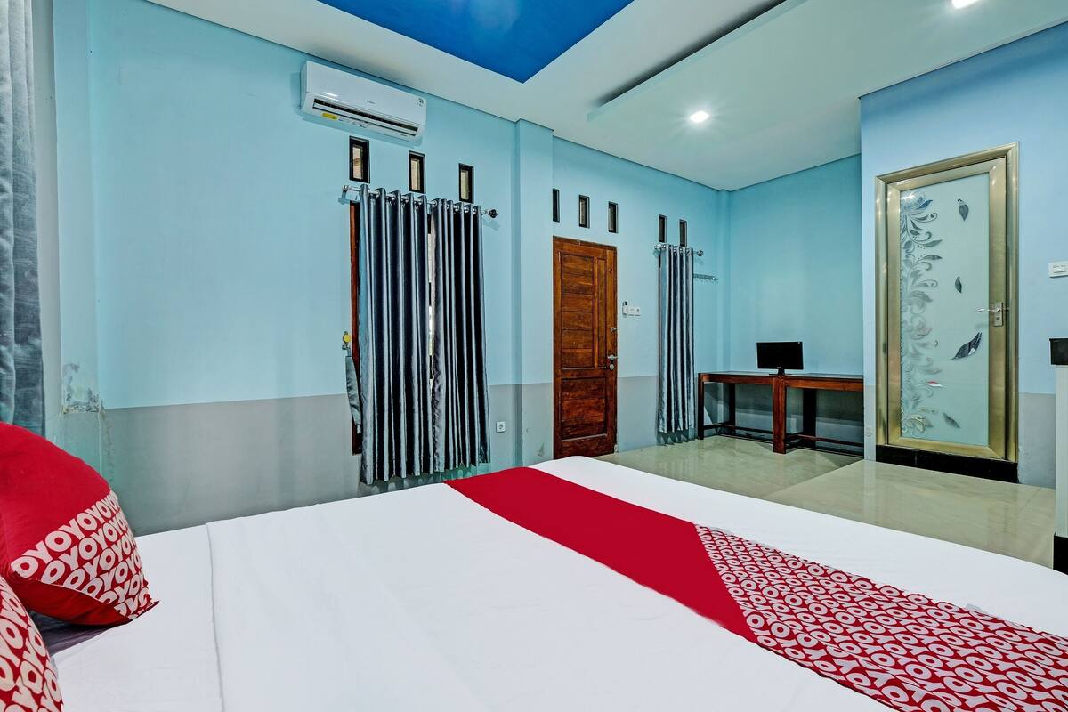 Una habitación de hotel con cama, una puerta de madera, un equipo de aire acondicionado y una mesita.