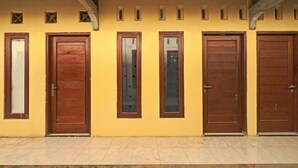 A row of wooden doors with glass panels, set against a yellow wall with small decorative windows. - OYO 91987 Archery Residence Syariah (Sewon)