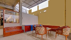 A room with a concrete floor, wooden bench, and a table with chairs. There is a window with a metal frame and a view of the outside. - OYO 91987 Archery Residence Syariah (Sewon)