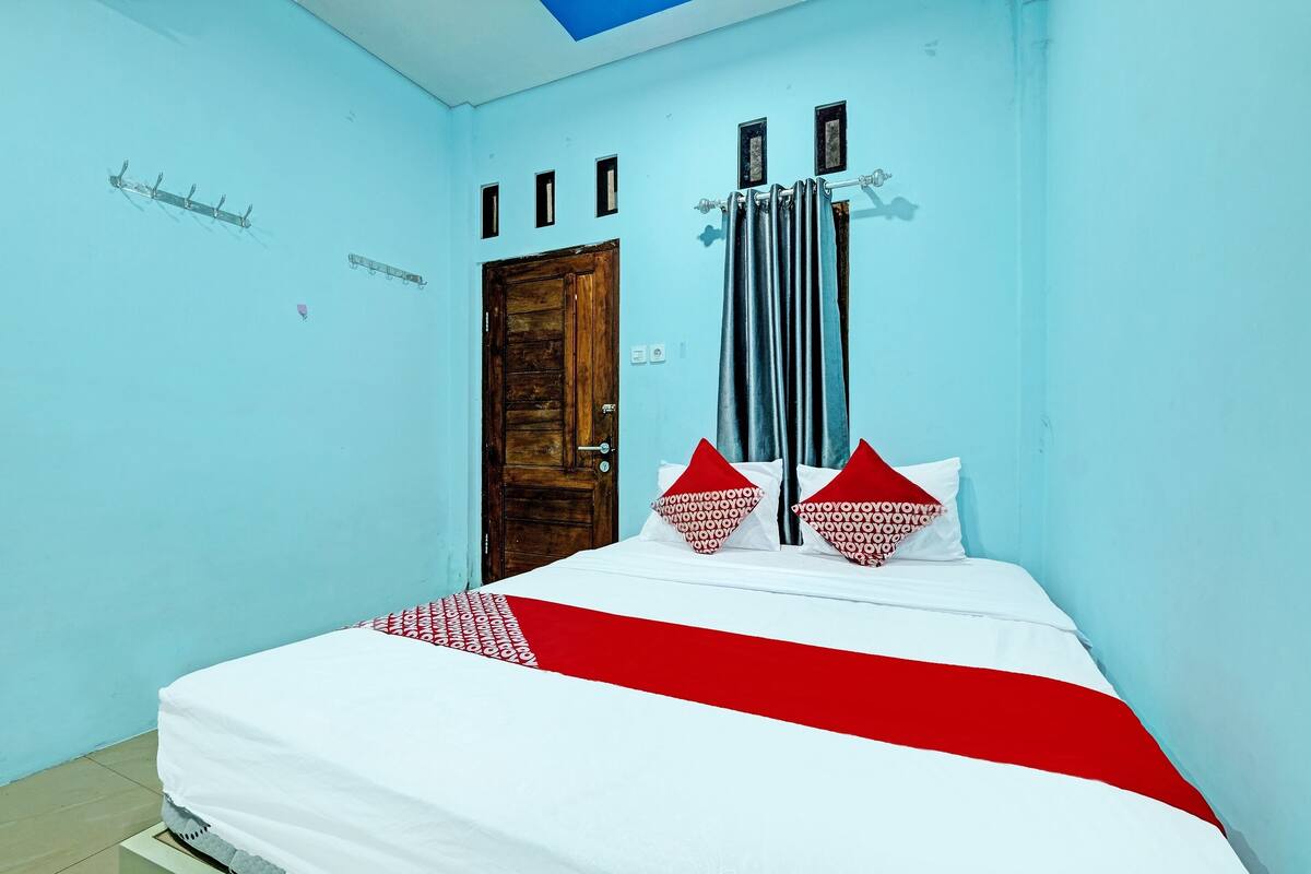 Un dormitorio con una cama, una puerta de madera y un ventanal con cortinas.