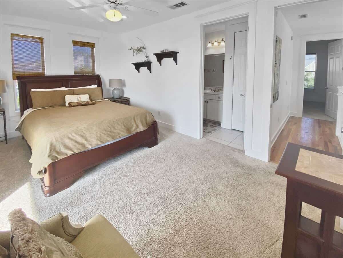 Un dormitorio con una cama grande, una mesita de noche, un aparador, una silla y una puerta que da al baño.