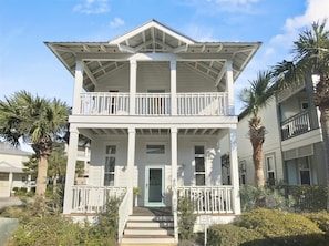 A two-story white building with a balcony, a front door, and a staircase leading to the entrance. - Across from Lagoon Pool in Seacrest Beach (Panama City Beach)