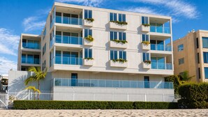 A multi-story building with balconies, a white facade, and a sandy ground. - Bay-view 2BR condo in Crown Point with pool, patio, and beach access. (San Diego)