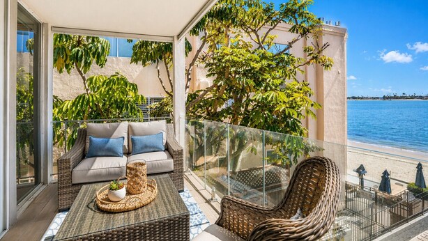 A balcony with a wicker sofa, a small table with a plant, and a wicker chair. - Bay-view 2BR condo in Crown Point with pool, patio, and beach access. (San Diego)