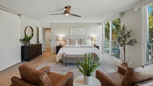 A spacious bedroom with a large bed, a ceiling fan, and a view of the outdoors through large windows. - Bay-view 2BR condo in Crown Point with pool, patio, and beach access. (San Diego)