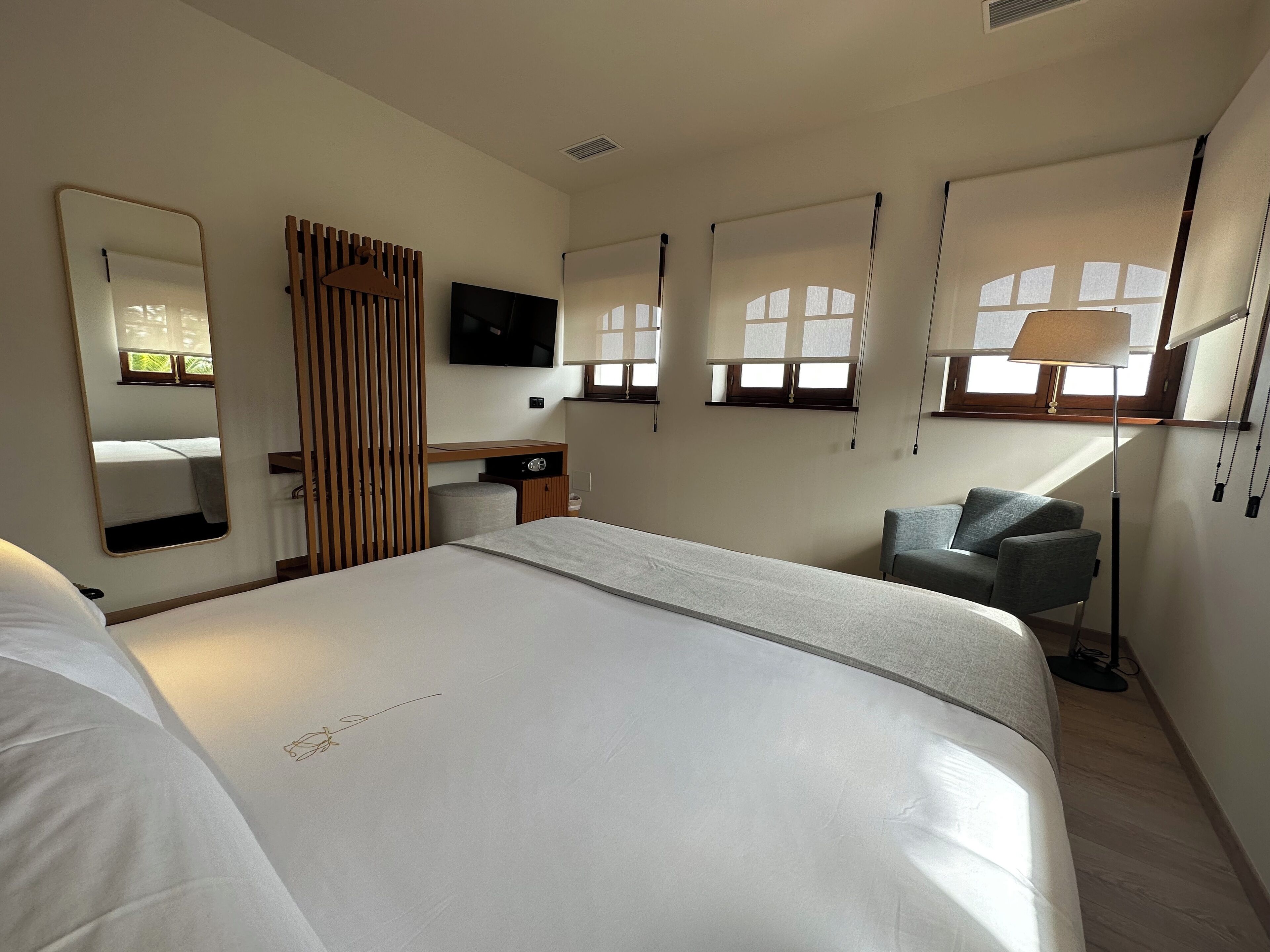 A hotel room with a large bed, a desk, a chair, a TV, and a window with a view.