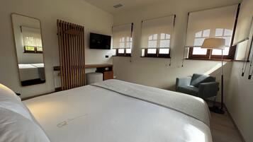 A hotel room with a large bed, a desk, a chair, a TV, and a window with a view.