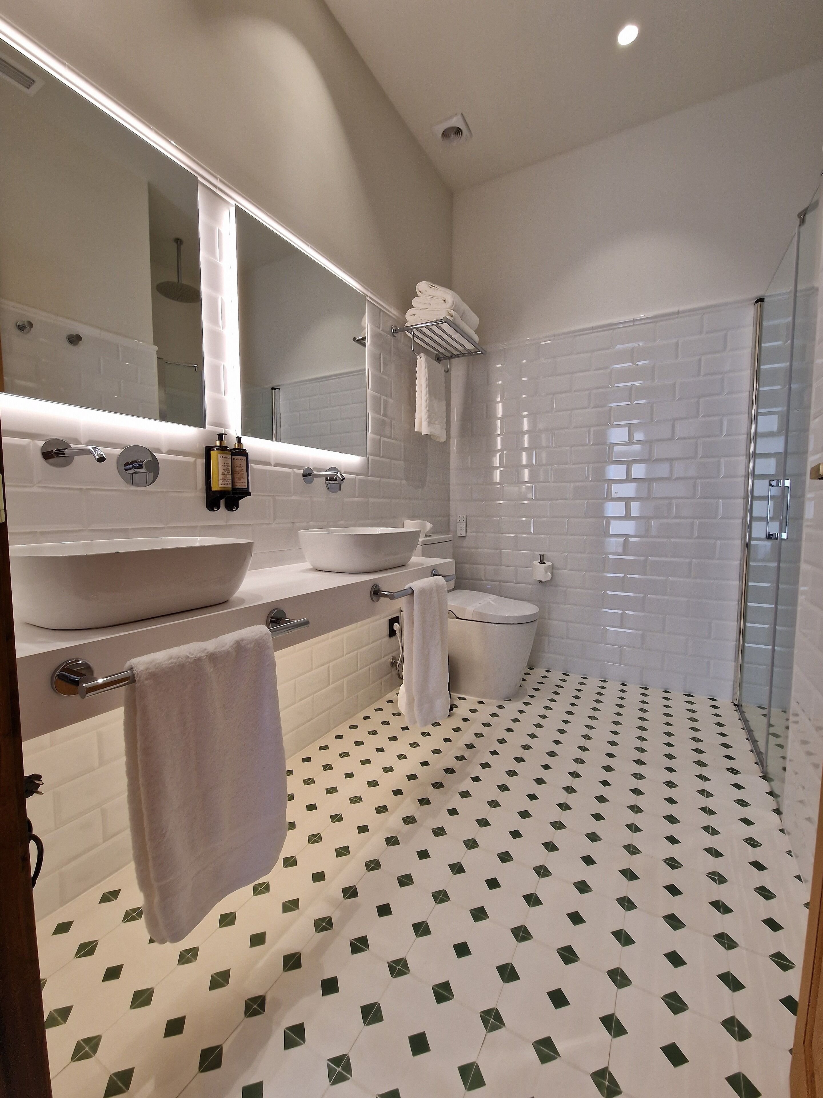 A modern bathroom with a large mirror, two sinks, a toilet, and a shower.