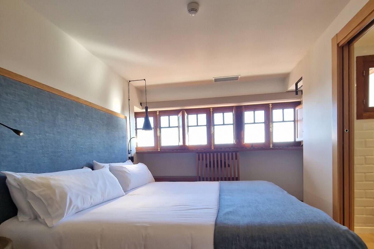A bedroom with a bed, a window with a view, a radiator, and a door.