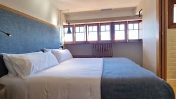 A bedroom with a bed, a window with a view, a radiator, and a door.
