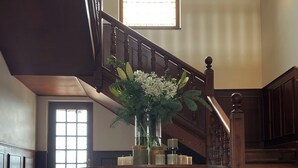 Una amplia escalera con detalles de madera que conduce a un piso superior. En la base, una mesa de madera con un jarrón de flores.