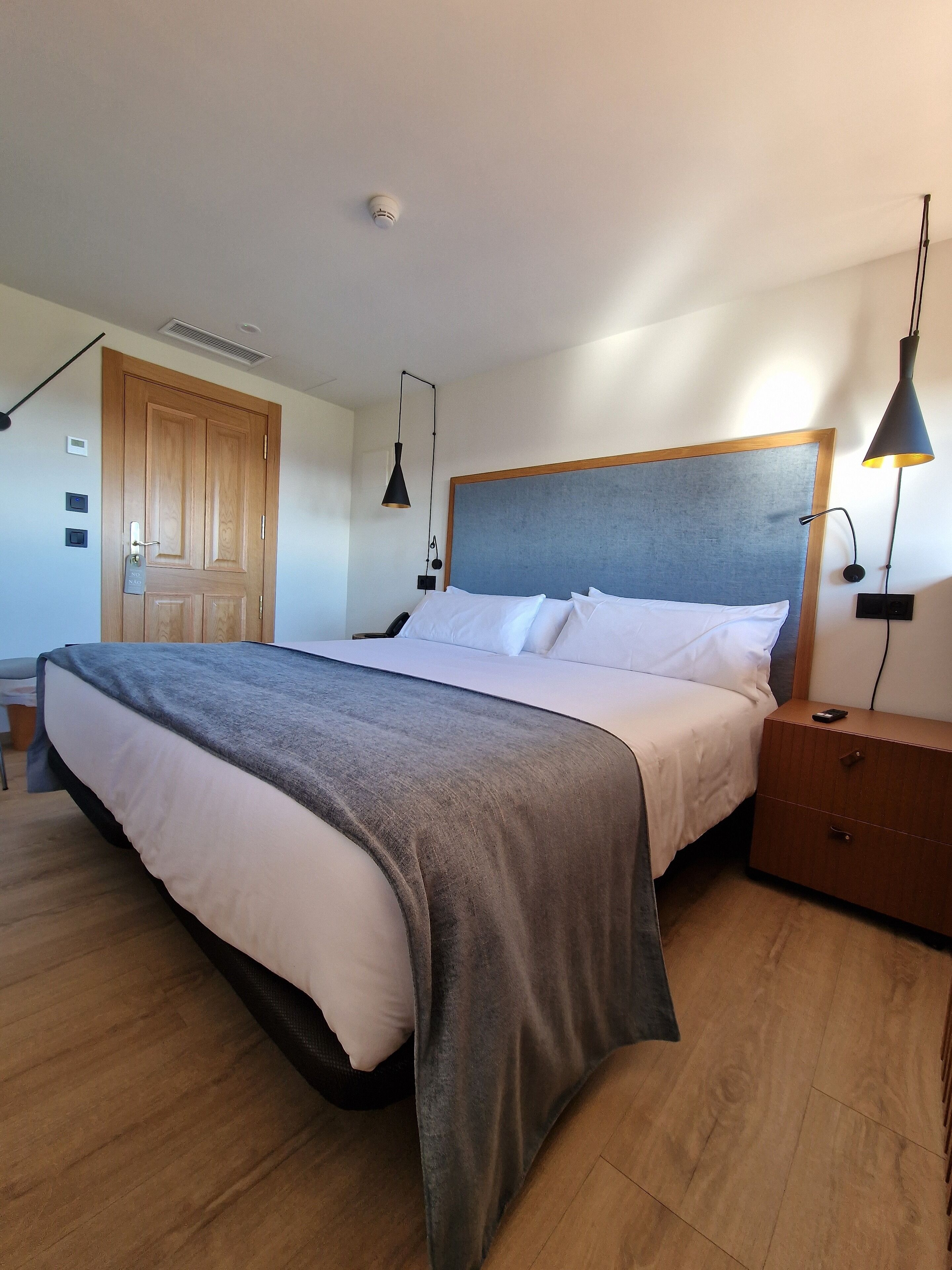 Un dormitorio con cama, mesitas de noche, armario, puerta y una lámpara en el techo.