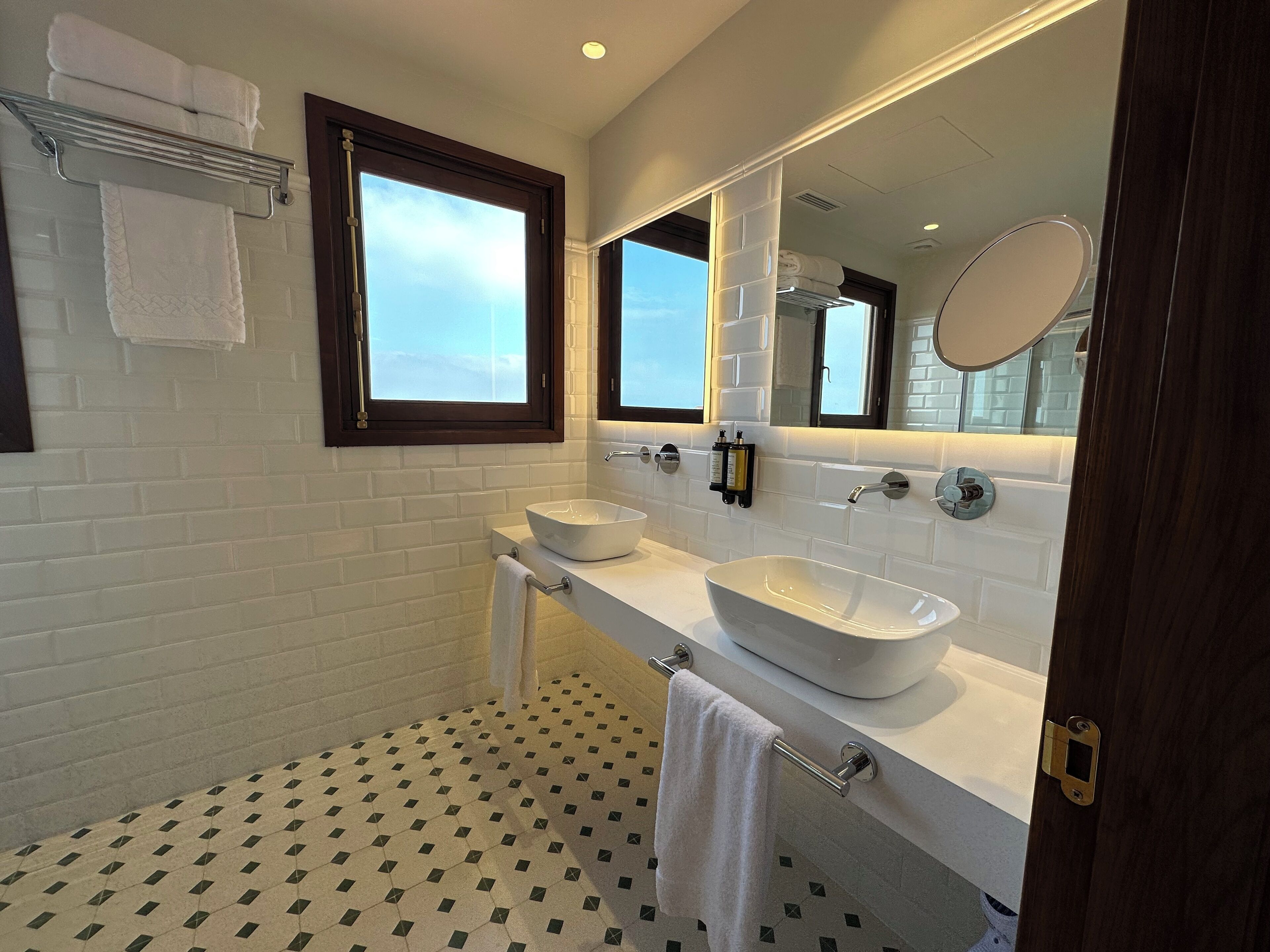 A modern bathroom with a white sink, a large mirror, and a window.