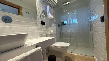 Un bany modern amb dutxa amb envàs de vidre, un lavabo blanc i un vàter.