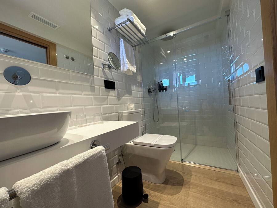 Un bany modern amb dutxa amb envàs de vidre, un lavabo blanc i un vàter.