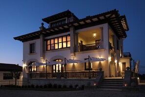 A two-story building with a balcony, outdoor seating area, and a staircase leading to the entrance.