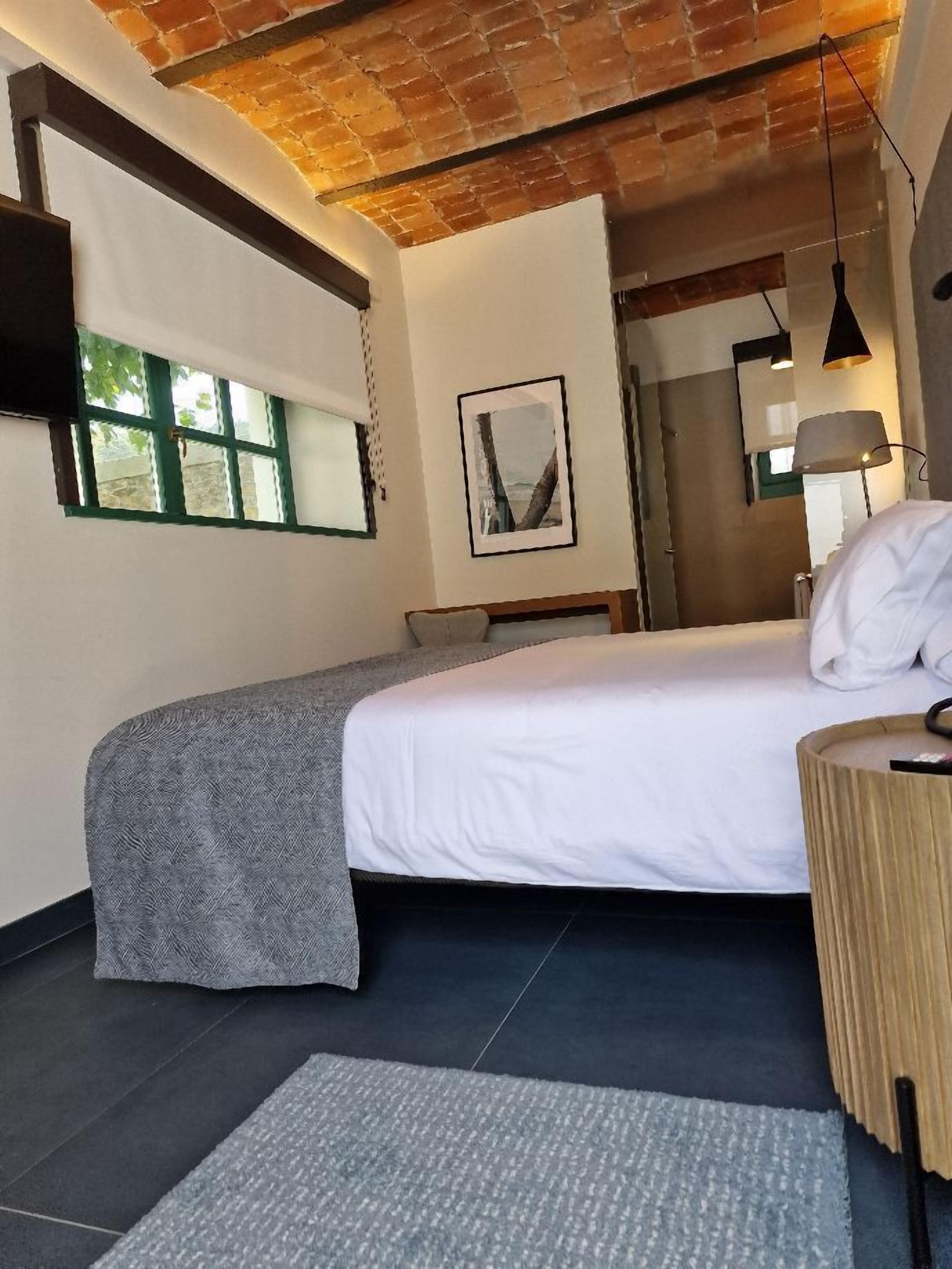 Un dormitorio moderno con una cama grande, un escritorio pequeño, una silla, una lámpara y una ventana.