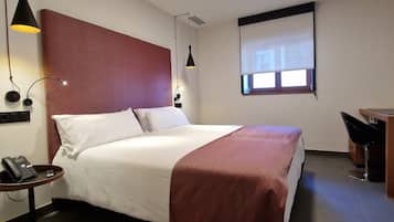 Una habitación de hotel con cama, mesita de noche, lámpara y un escritorio con silla.