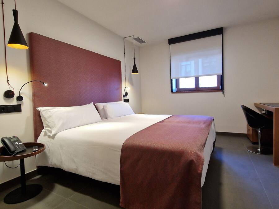 Una habitación de hotel con cama, mesita de noche, lámpara y un escritorio con silla.