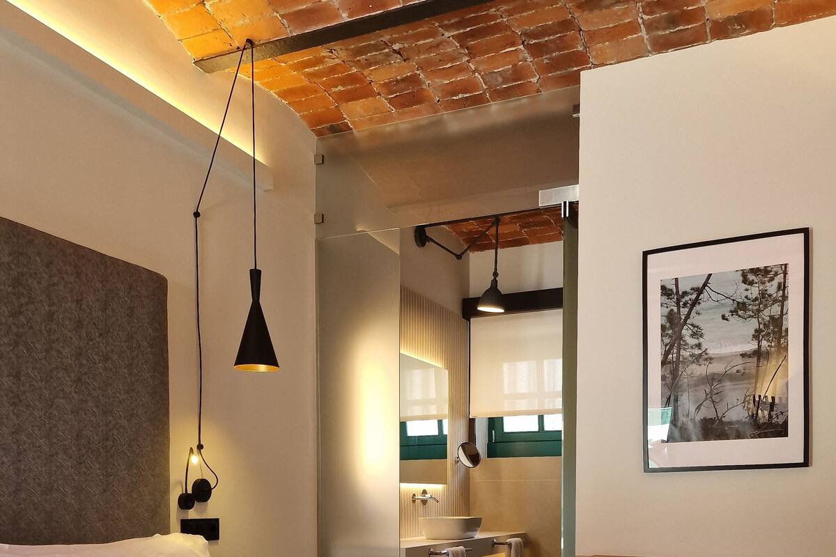 A hotel room with a bed, a desk, a chair, a bathroom with a mirror, and a framed picture on the wall.