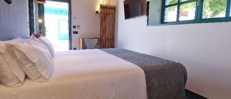 Un dormitorio con una cama, un televisor montado en la pared, una ventana y un techo con ladrillo a la vista.