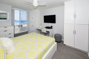 A bedroom with a bed, a desk, a television, and a view of the ocean.