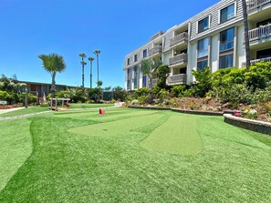 A well-maintained courtyard with a putting green, surrounded by multi-story buildings with balconies and a clear blue sky.