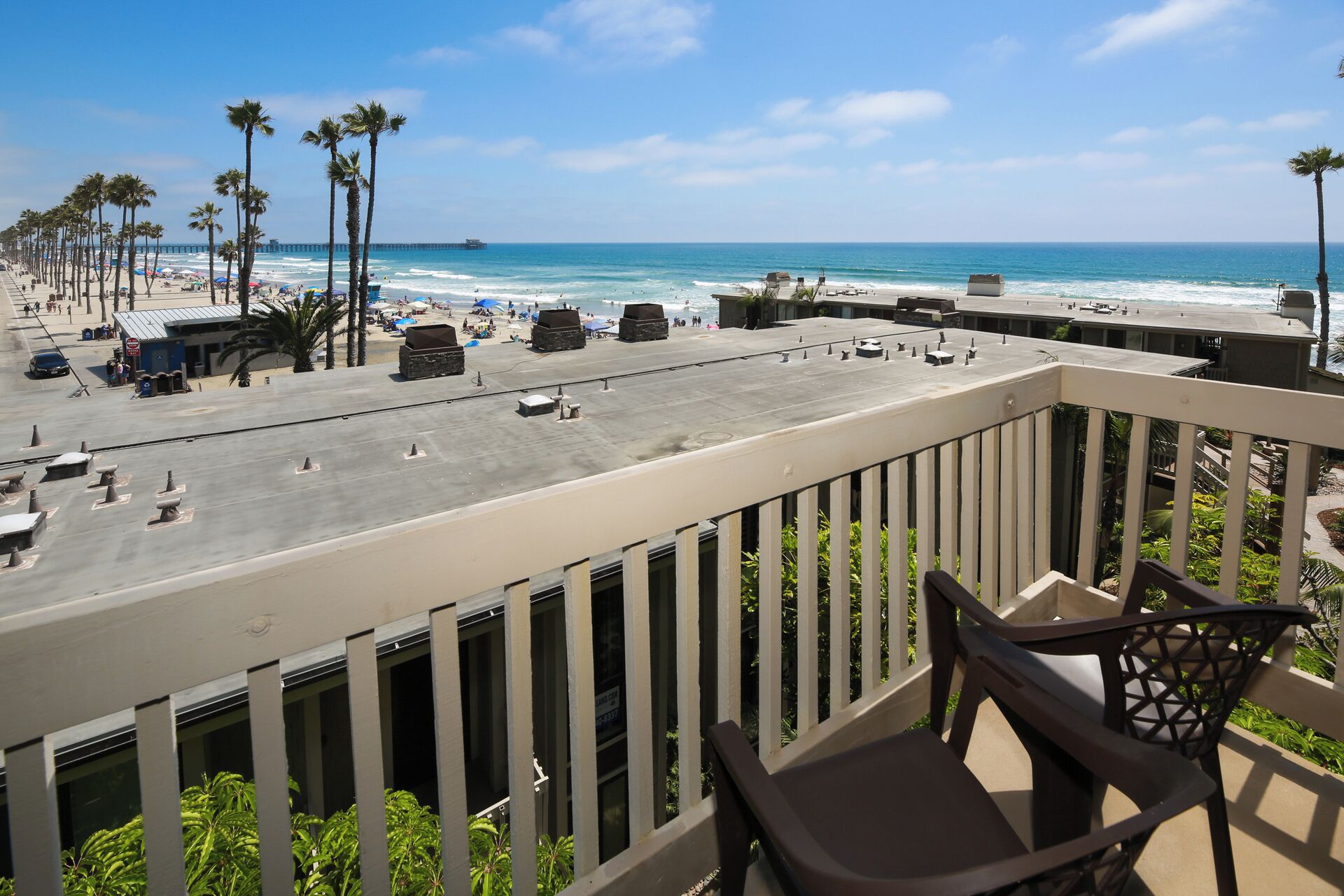 A balcony with a view of a beach, palm trees, and a pier in the distance.