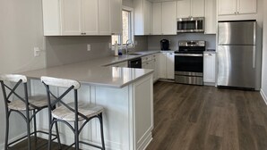 A modern kitchen with white cabinetry, stainless steel appliances, and a central island with bar stools.