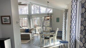 A dining area with a table set for two, a kitchen in the background, and a view of the living room through a glass door.