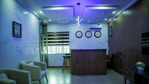 A modern living room with a wooden reception desk, two sofas, a coffee table, and a TV on a wooden cabinet. - Bethel Hotel and Suites (Abuja)