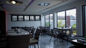 A modern dining area with tables and chairs, large windows, and a view of the outside. - Bethel Hotel and Suites (Abuja)