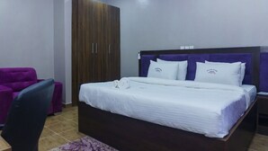 A bedroom with a bed, a purple chair, and a wardrobe. - Bethel Hotel and Suites (Abuja)