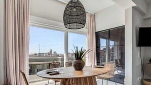 A modern dining area with a round table, chairs, a potted plant, and a city view. - Sanders Old Port - Lovely 1-bdr. Apt (Thessaloniki)