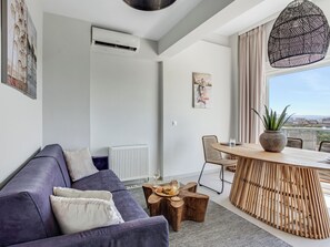 Een moderne woonkamer met een bank, een eettafel met stoelen, een potplant en uitzicht op de stad.