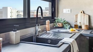 A modern kitchen with a black sink, a window, a potted plant, and a wooden cutting board. - Sanders Old Port - Lovely 1-bdr. Apt (Thessaloniki)