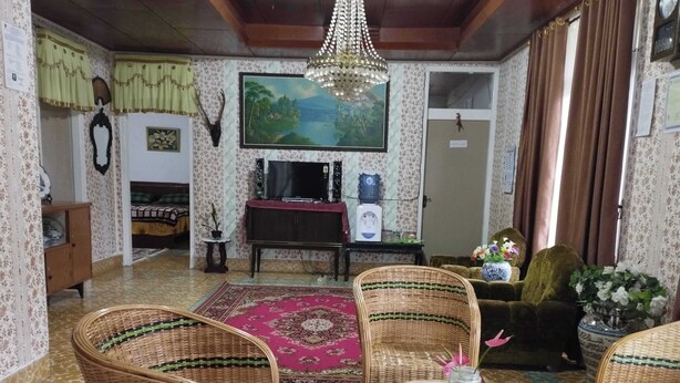 A living room with wicker furniture, a television, a painting, and a chandelier. - EXPRESS O 92070 Mando Homestay Syariah Near KANTOR LURAH Bukik Apik Puhun (Bukittinggi)