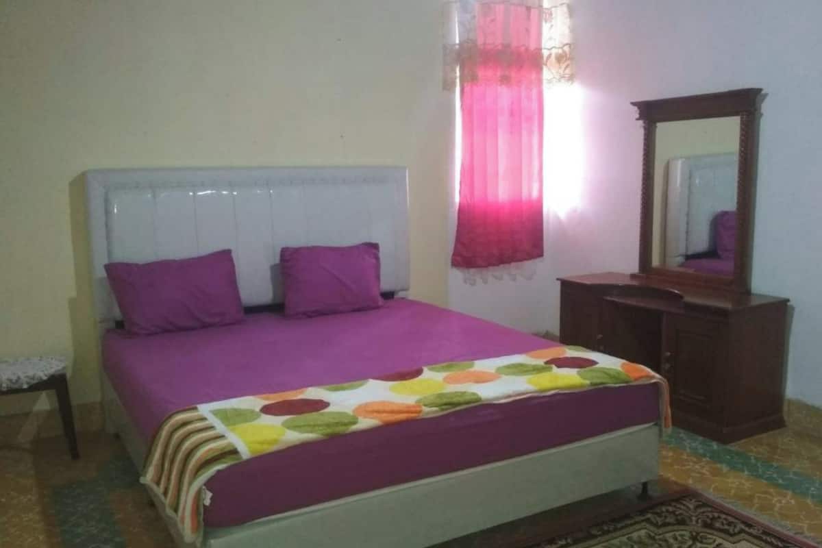 A bedroom with a bed, a dresser, a mirror, and a window with curtains.