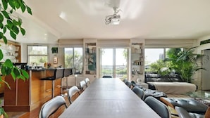 Un espace repas moderne comprenant une longue table, des chaises et un coin cuisine avec un comptoir et des placards.